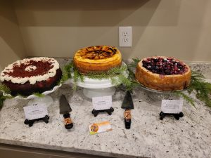 Three cheesecakes are displayed on stands decorated with greenery.