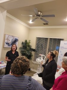 A dark haired woman speaks to a group of women about medical spa treatments.